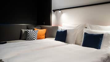 A neatly made bed with white and blue pillows, a grey headboard, and a black wall with a light fixture.