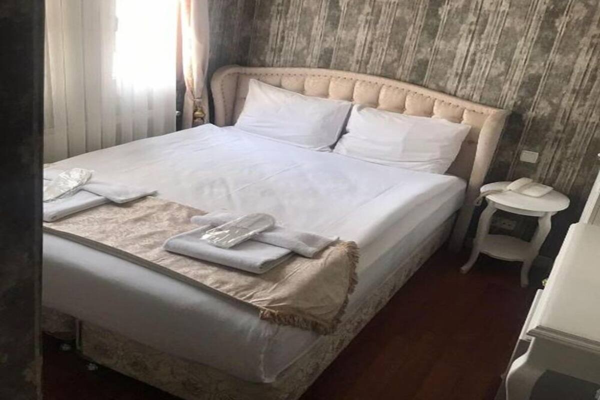 A neatly made bed with white linens and pillows, a bedside table with a phone, and a small round table with a lamp.