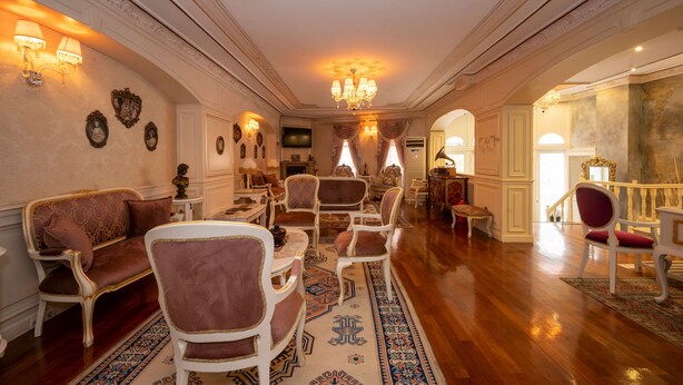 A spacious room with a wooden floor, a sofa, multiple chairs, a chandelier, and a television. - Fuat Bey Palace Hotel (Istanbul)