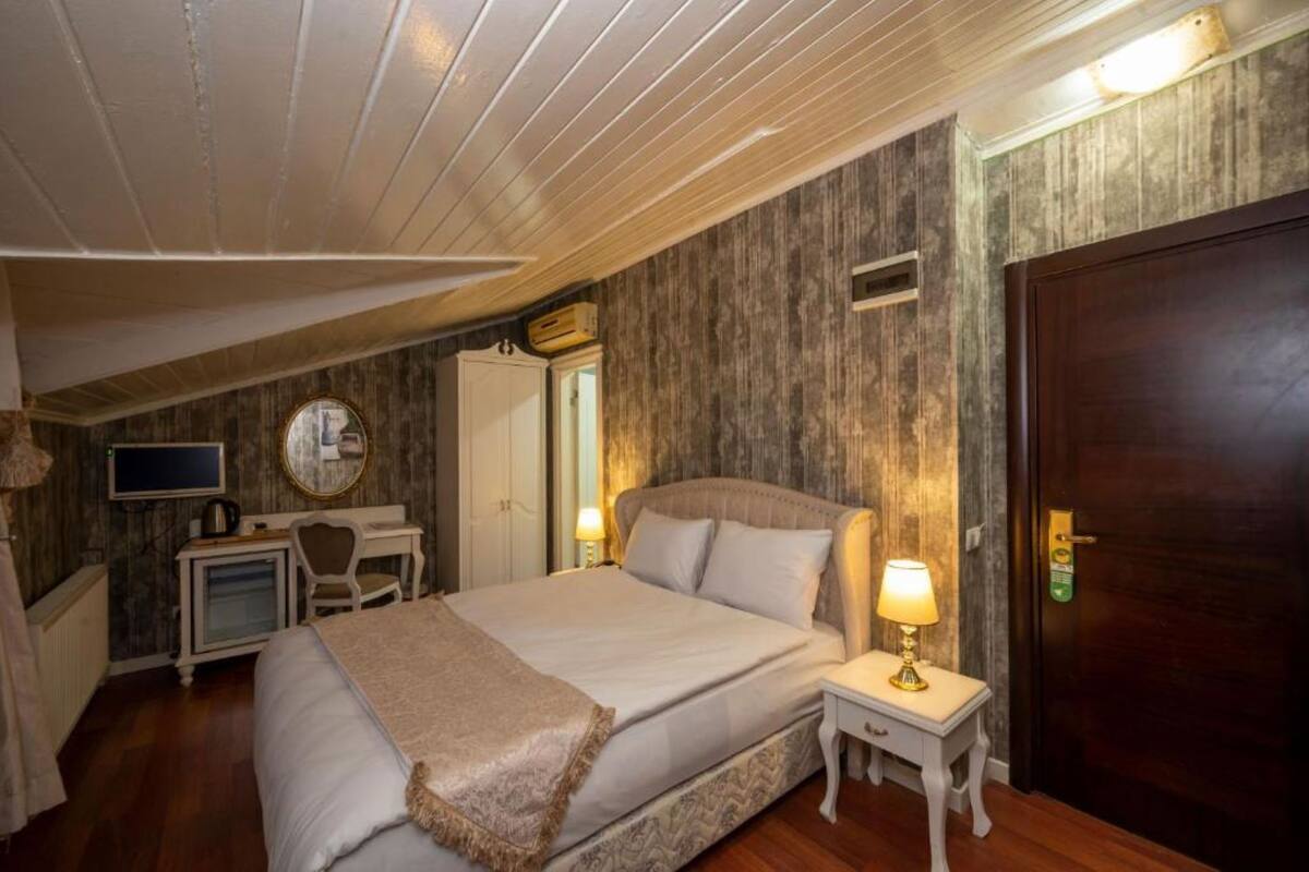 A bedroom with a bed, bedside table with a lamp, a desk with a chair, a wardrobe, and a door.