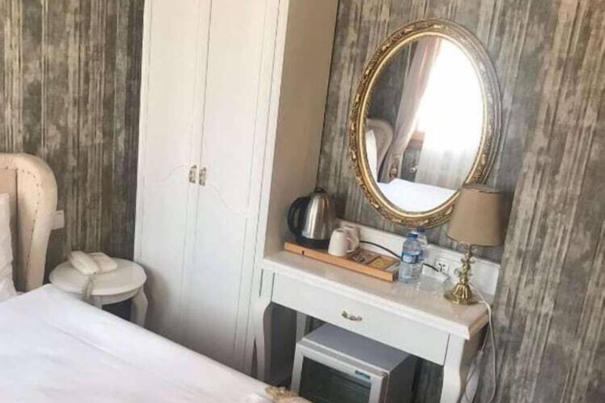 A hotel room with a bed, a wardrobe, a vanity with a mirror, a small desk, and a trash bin.