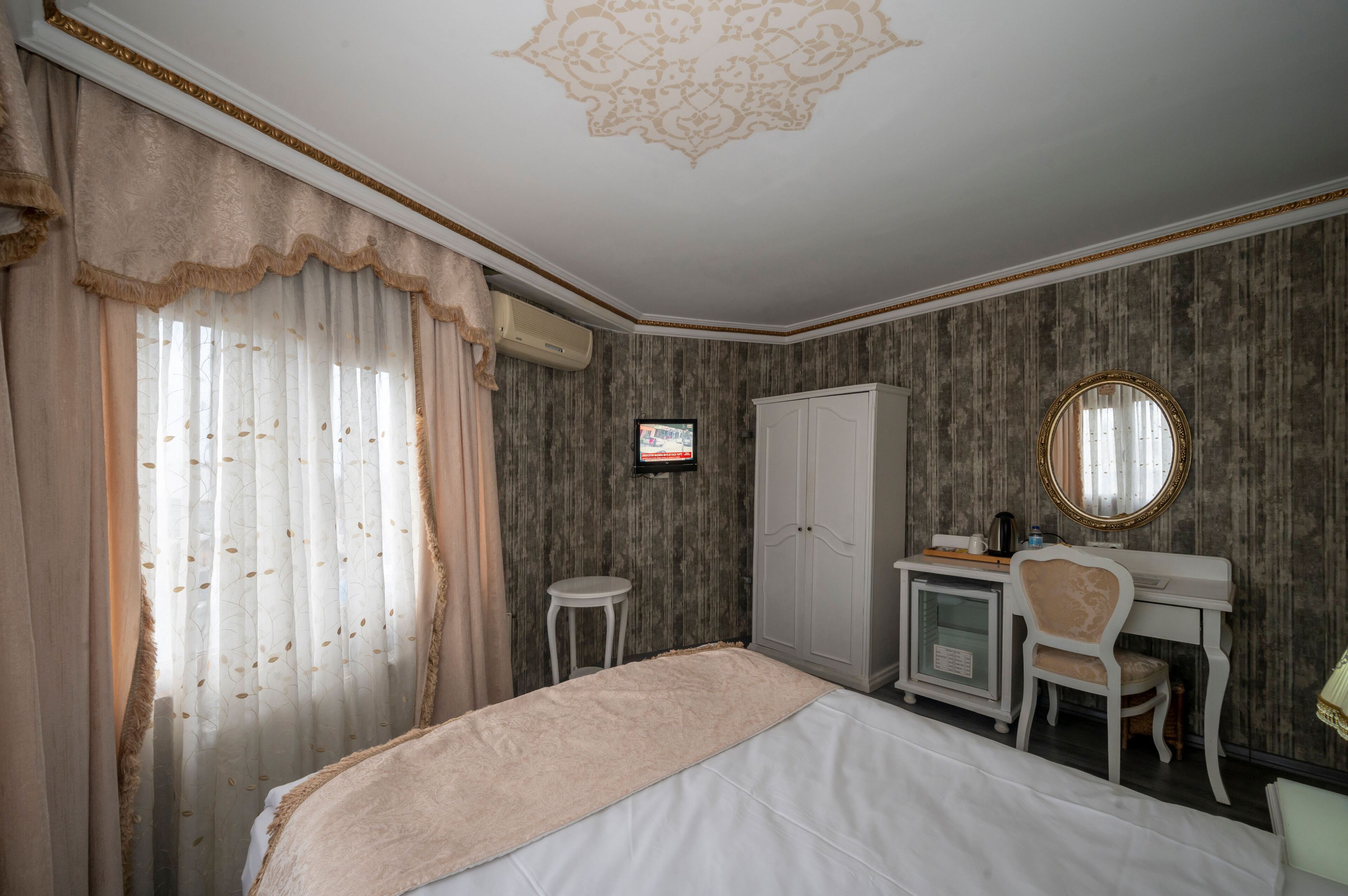 A bedroom with a bed, a desk, a chair, a wardrobe, a television, and a mirror.