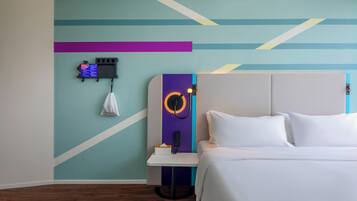 A modern hotel room with a neatly made bed, a small bedside table with a lamp, and a wall-mounted phone.