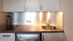 Une cuisine de taille réduite, dotée d’appareils électroménagers en acier inoxydable, d’un évier et d’un égouttoir à vaisselle.