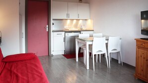 Un espace de vie compact comprenant un coin cuisine, un coin repas avec des chaises blanches et une porte rouge.