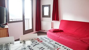 Une chambre d’hôtel avec un canapé rouge, un téléviseur posé sur un meuble en bois et une fenêtre ornée de rideaux rouges.