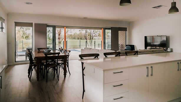 A modern kitchen with a dining area, large windows, and a TV. - A Brand New Home with a Pool overlooking The Black Bull Golf Course (Yarrawonga)