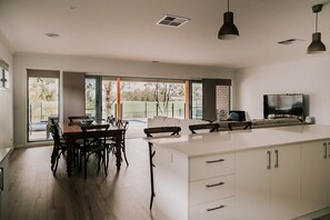 A modern kitchen with a dining area, large windows, and a TV. - A Brand New Home with a Pool overlooking The Black Bull Golf Course (Yarrawonga)