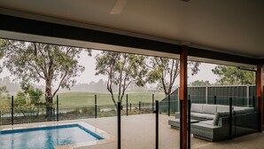A modern outdoor patio with a pool, a sofa, and a view of a grassy field. - A Brand New Home with a Pool overlooking The Black Bull Golf Course (Yarrawonga)