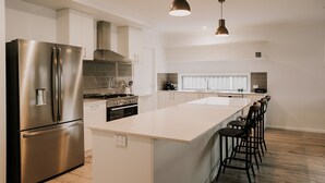 A modern kitchen with a stainless steel refrigerator, a gas stove, and a large island with bar stools. - A Brand New Home with a Pool overlooking The Black Bull Golf Course (Yarrawonga)
