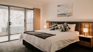 A bedroom with a large bed, two bedside tables with lamps, a ceiling fan, a sliding glass door leading to an outdoor area, and a painting on the wall. - A Brand New Home with a Pool overlooking The Black Bull Golf Course (Yarrawonga)