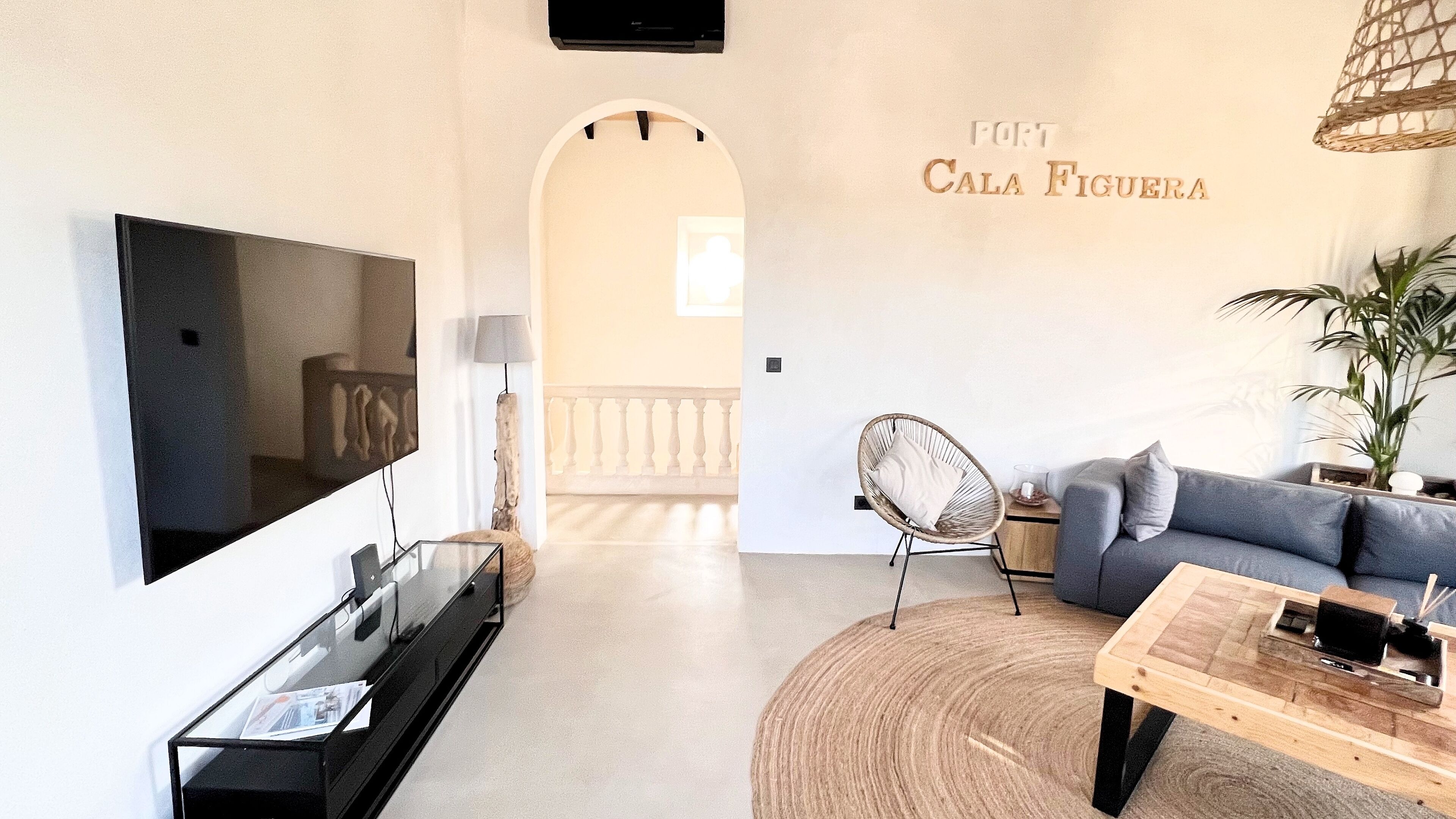 Un salon moderne avec un téléviseur à écran plat, un canapé gris, un fauteuil en osier et une table basse en bois.