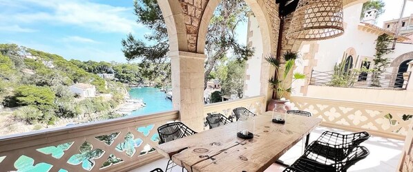 Una terraza con mesa y sillas de madera, con vista a una piscina y vegetación.