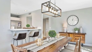 A modern dining area with a wooden table, black chairs, and a hanging light fixture.