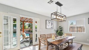A dining area with a wooden table and chairs, a hanging light fixture, and a view of an outdoor patio with a pool.