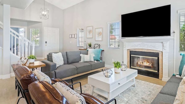 A modern living room with a fireplace, a large flat-screen TV, a grey sofa, leather chairs, and a white coffee table.