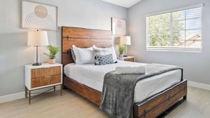 A bedroom with a wooden headboard, a large bed with white bedding, two bedside tables with lamps, and artwork on the walls.