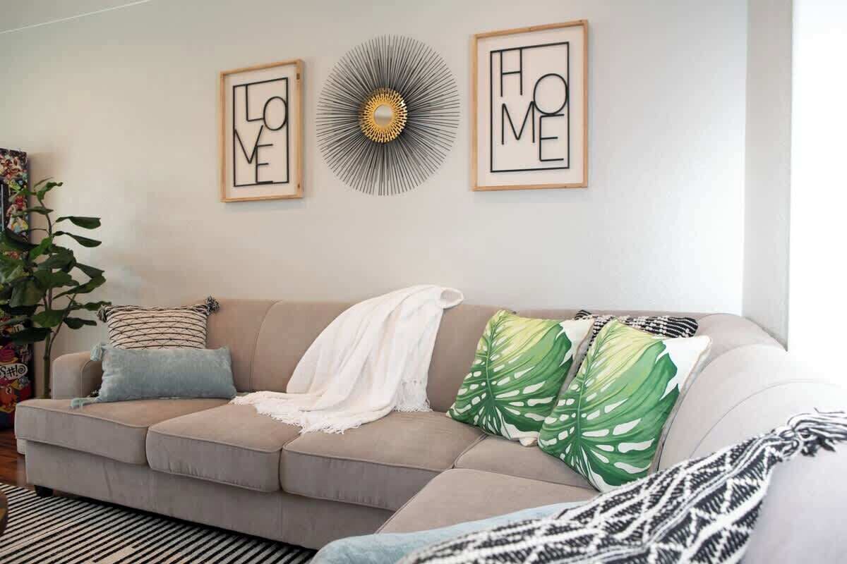 Ett vardagsrum med en beige soffa, en mönstrad pläd och en stor, grön, lövformad prydnadskudde.