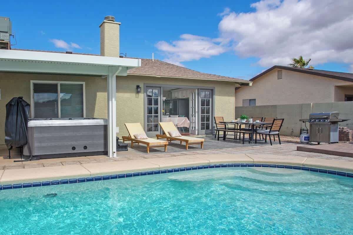 Een achtertuin met een zwembad, lounge stoelen, een jacuzzi en een barbecue.