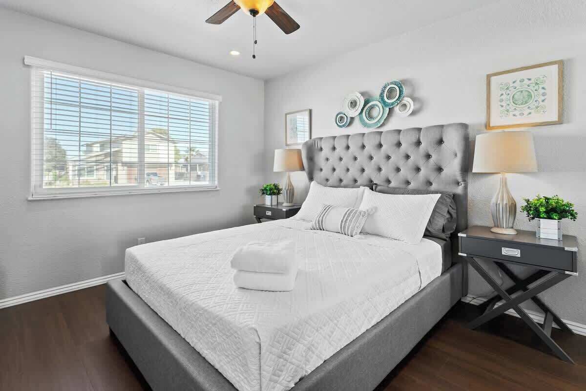 Quarto com uma cama grande, um ventilador de teto, uma janela com persianas e arte decorativa na parede.