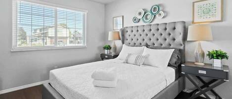 Quarto com uma cama grande, um ventilador de teto, uma janela com persianas e arte decorativa na parede.