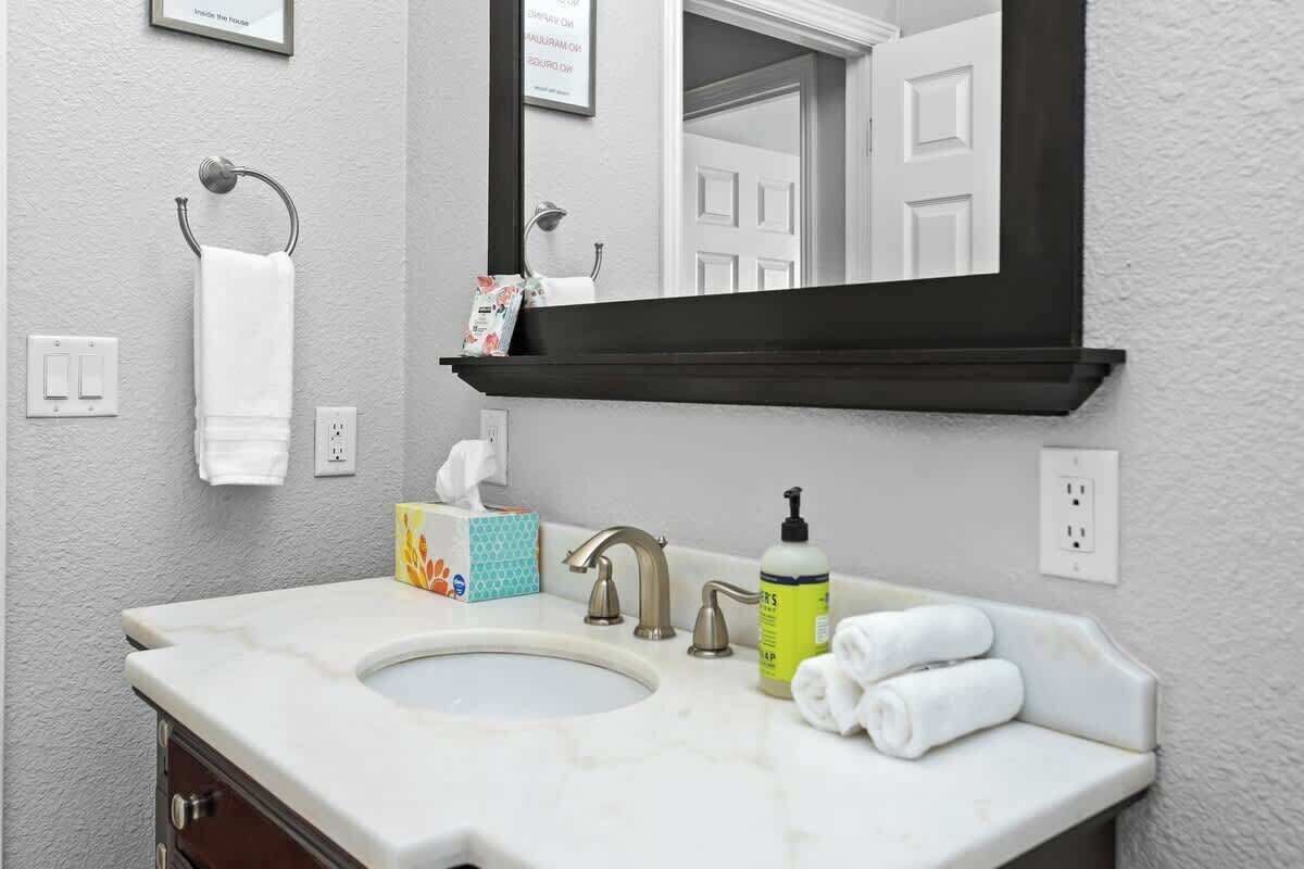 A bathroom with a white sink, a mirror, a towel rack, and a box of tissues.