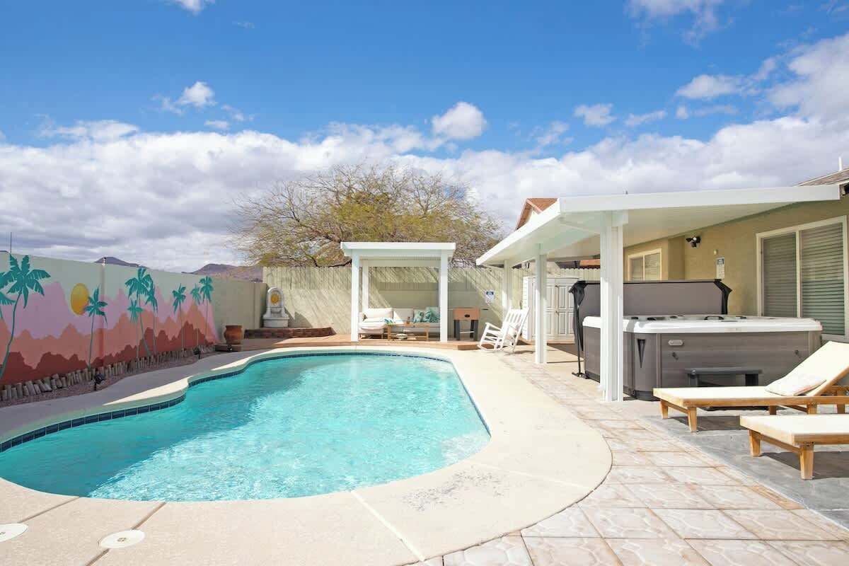 A swimming pool with lounge chairs, a hot tub, and a covered seating area.