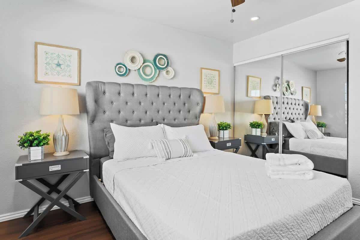 A modern bedroom with a tufted headboard, a large mirror, and a neatly made bed with white linens.