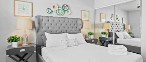 A modern bedroom with a tufted headboard, a large mirror, and a neatly made bed with white linens.