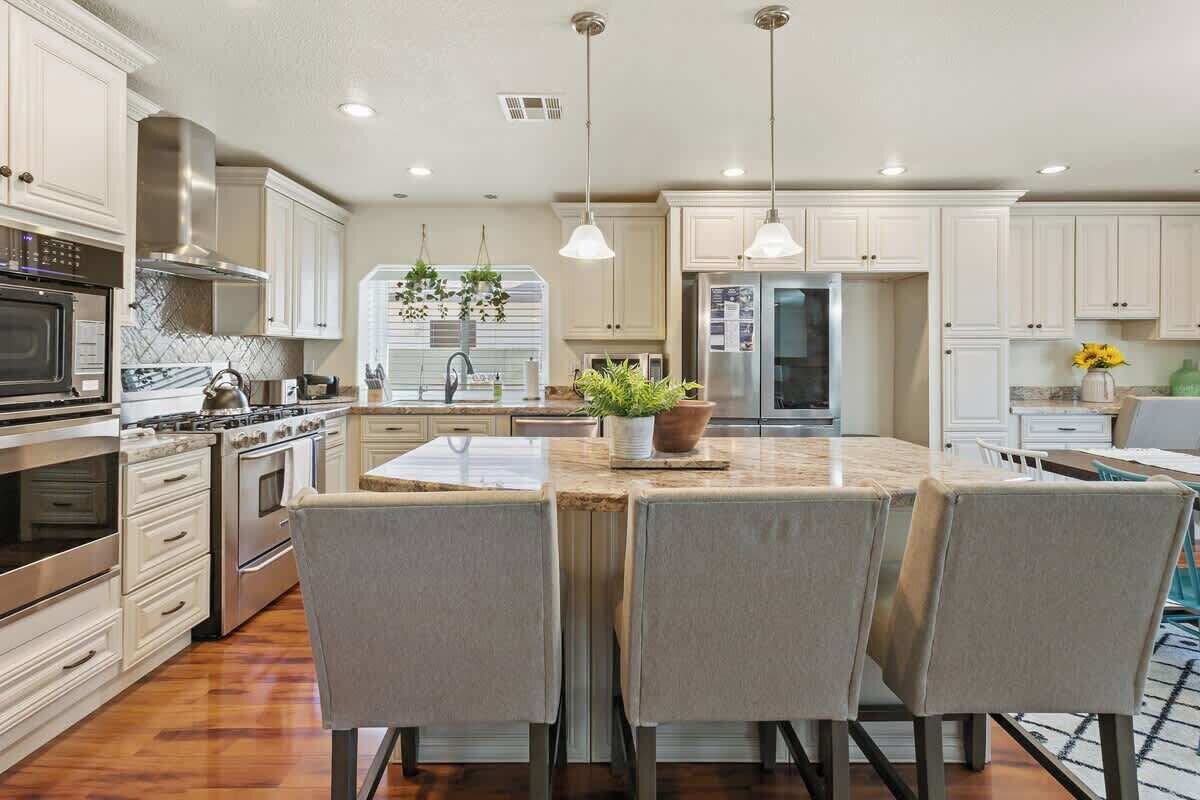 A modern kitchen with white cabinetry, stainless steel appliances, and a central island with chairs.
