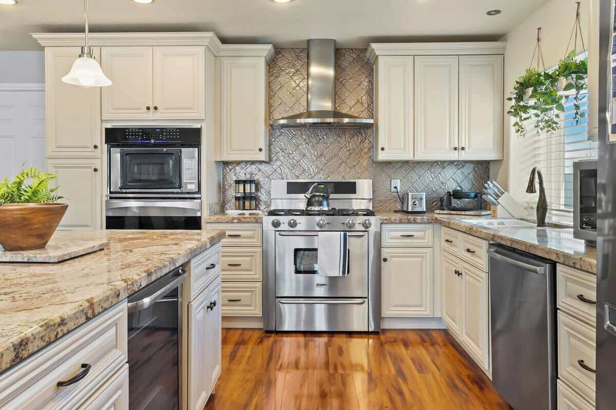 A modern kitchen with white cabinets, stainless steel appliances, and a wooden floor.