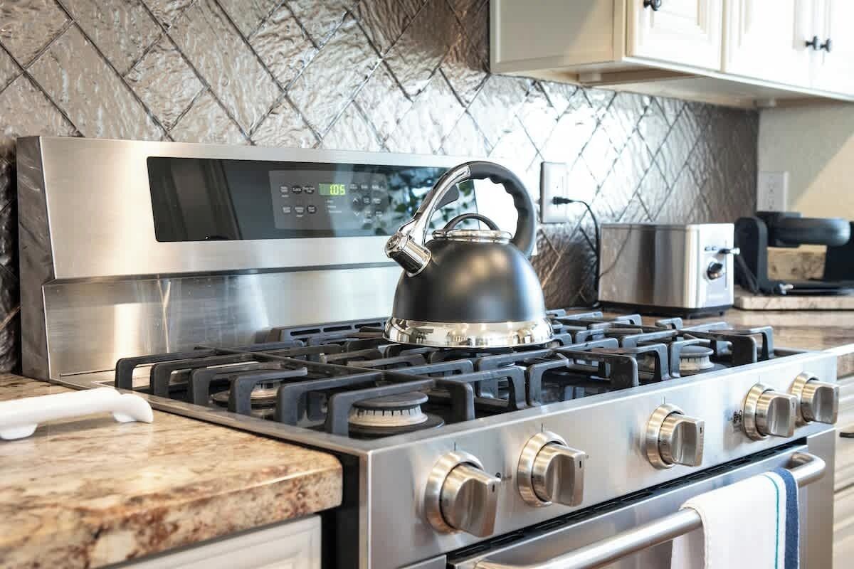 A stainless steel stove with a digital control panel and a kettle on top.