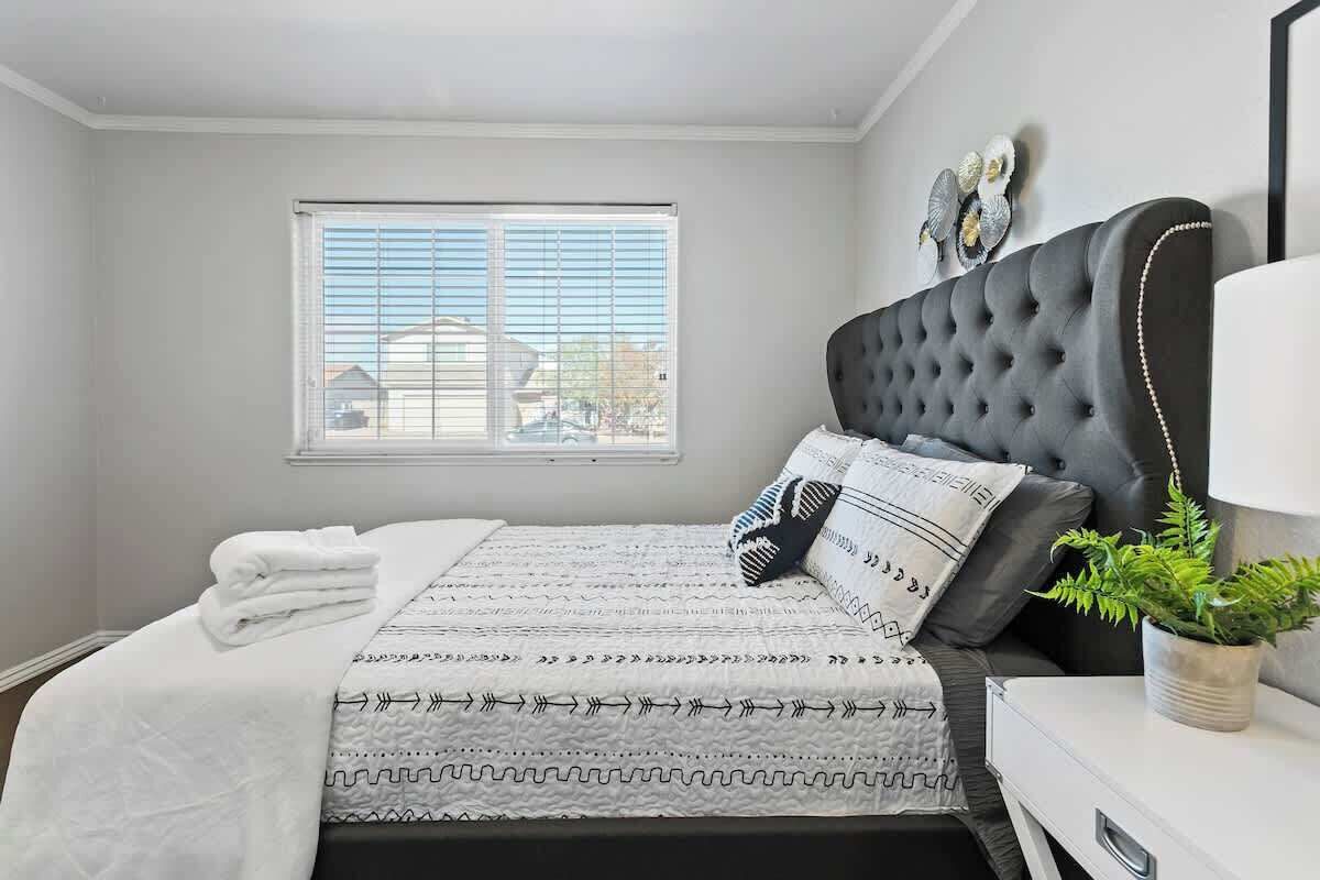 A neatly made bed with a patterned bedspread, a bedside table with a lamp, and a window with blinds.