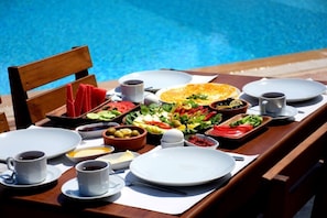 A dining table with a variety of breakfast items and a pool in the background. - Levia Hotel (Cesme)