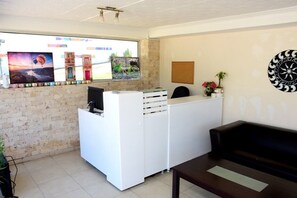 Zona de recepción con un escritorio blanco, un sofá negro y una obra de arte colgada en la pared.