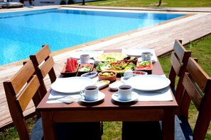 Une table à manger avec des assiettes, des tasses et une variété d’aliments, installée à l’extérieur, près d’une piscine.