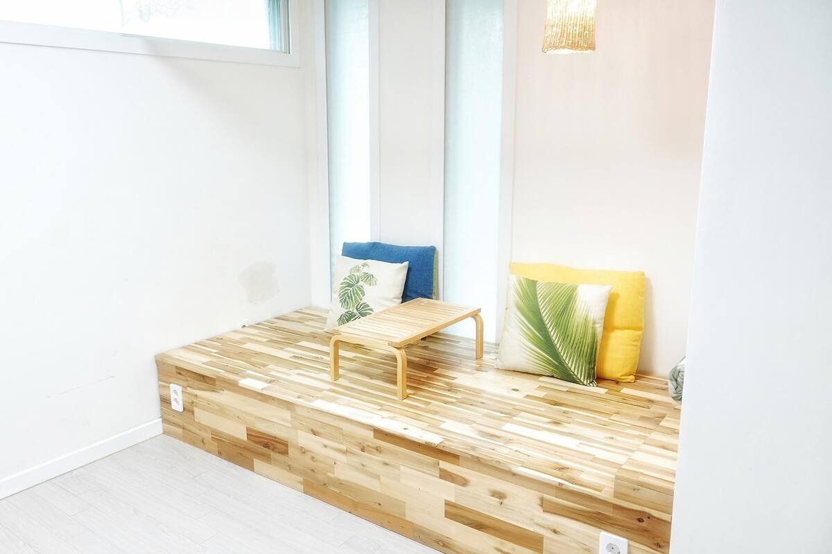 Ein Zimmer mit einer Holzplattform, einem kleinen Tisch und einem blauen Sofa mit gemusterten Kissen.