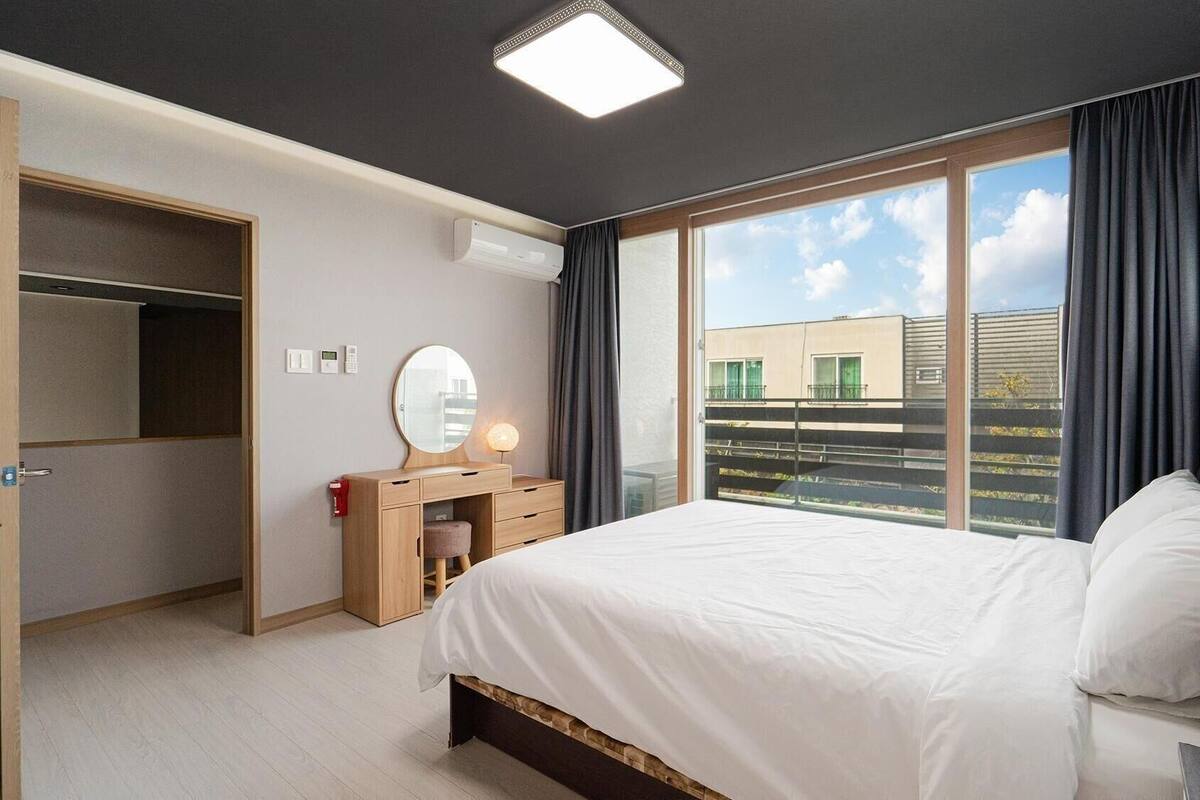 Ein Schlafzimmer mit Bett, Schminktisch, Spiegel und einem Fenster mit Vorhängen.
