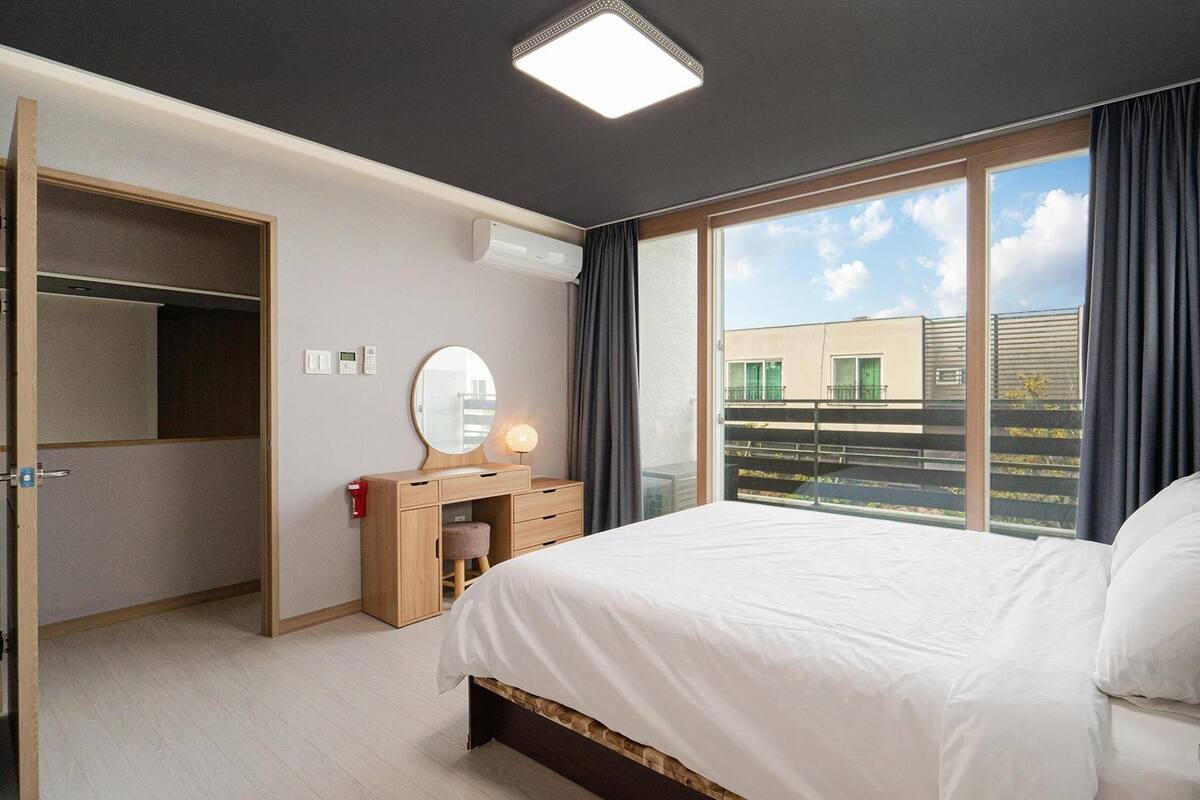 Ein Schlafzimmer mit Bett, Kommode, Spiegel und einem Fenster mit Vorhängen.