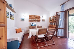 A cozy room with a bed, a dining table with chairs, a TV, and a bookshelf.