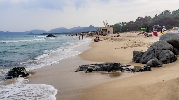 A beach with clear skies, calm waters, and rocky outcrops.