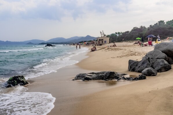 A beach with clear skies, calm waters, and rocky outcrops.