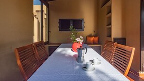 A dining area with a table set for two, a coffee pot, cups, and a vase with flowers.