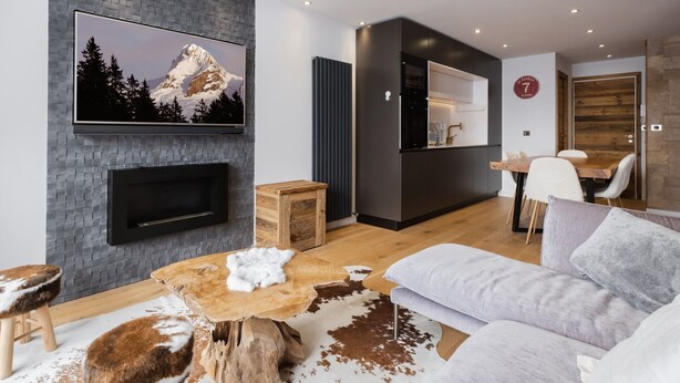 Ein modernes Wohnzimmer mit Kamin, einem Wandfernseher, einem Essbereich und einer Küche.