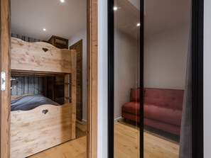A wooden bunk bed with a ladder, a red sofa, and a glass partition. - 4★ South-Facing Apt, 6 pers, 2 bdrms, La Clusaz with balcony (La Clusaz)