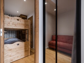 Una cama nido de madera con una escalera, un sofá rojo y un separador de vidrio.