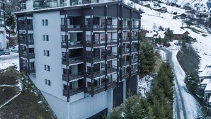 Ein mehrstöckiges Gebäude mit Balkonen in einer verschneiten Berglandschaft.