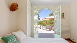 Une chambre avec un lit, un oreiller orné du mot « ALOHA », et une porte ouverte donnant sur une terrasse avec une chaise et un parasol.