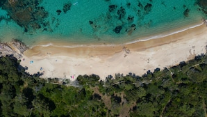 Vue aérienne d’une plage aux eaux turquoise et limpides, bordée d’un rivage sablonneux et d’une végétation luxuriante.
