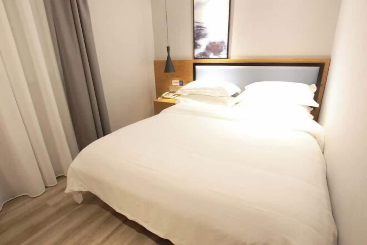 A hotel room with a bed, a nightstand, a lamp, and a painting on the wall.